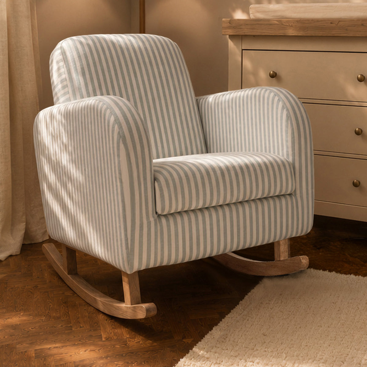 A striped upholstered rocking chair with curved arms and wooden rockers, shown in a softly lit room next to a dresser.