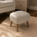 A small upholstered ottoman with cream and blue vertical stripes and light wood legs, shown in a styled room setting next to a matching striped armchair and a cream cabinet.