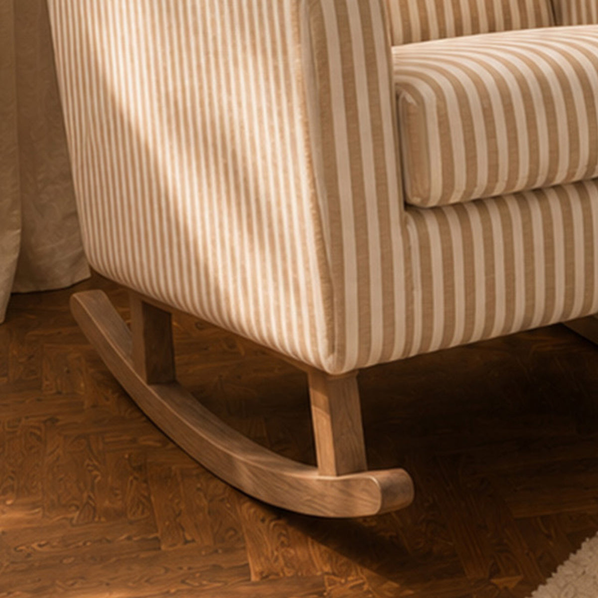 Close-up of a striped upholstered rocking chair with a curved wooden rocker base, shown on a dark wood herringbone floor.