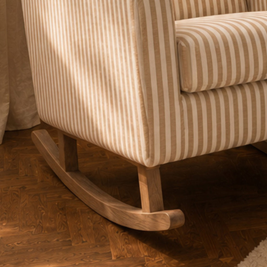 Close-up of a striped upholstered rocking chair with a curved wooden rocker base, shown on a dark wood herringbone floor.