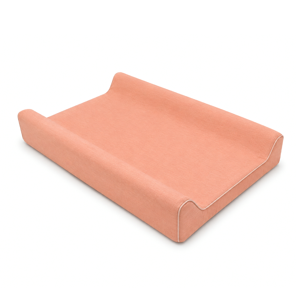 A peach-colored fabric changing pad or cushion with a contoured, tiered design and white contrast stitching, shown on a clean white background.