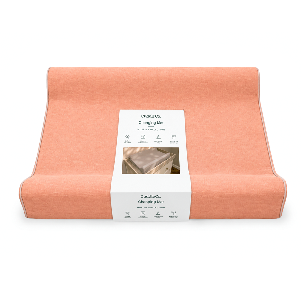 A folded peach-colored changing mat with a white paper label wrapped around the center, photographed on a clean white background.